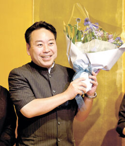 笑顔で花束を掲げる羽田さん（２０日午後８時５分、長野市内のホテル）