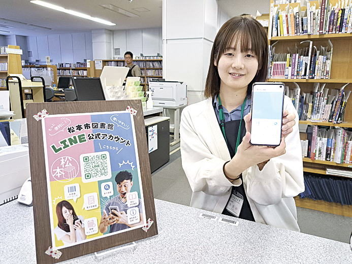 ライン公式アカウントをPRする図書館職員とカウンターに表示されたQRコード