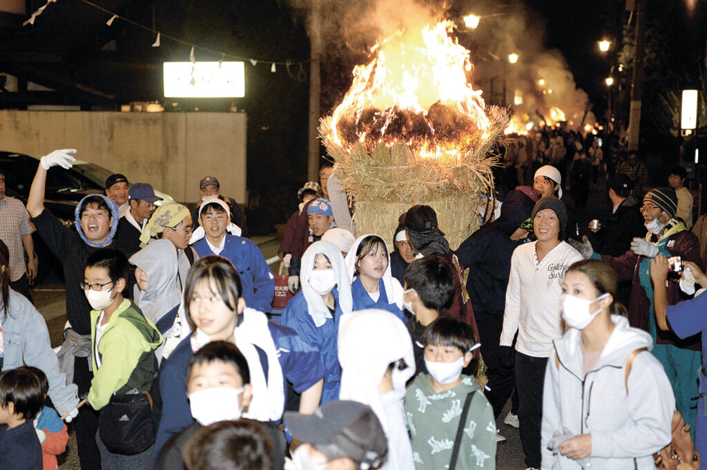 炎を上げるたいまつが温泉街を進み、大勢の人でにぎわう祭り